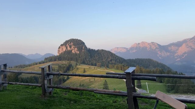 Peaceful alpine landscape at sunset featuring the Dietrichshorn mountain in Austria, rolling green meadows, wooden fence in foreground and soft evening light in the Alps.