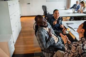Adult coworkers laughing at smartphone during coffee break in modern office