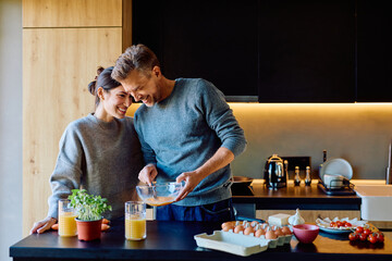 Cheerful couple preparing a healthy breakfast with eggs, vegetables, and orange juice, sharing a loving moment in a modern kitchen