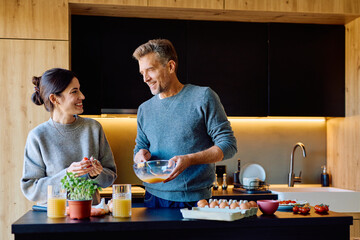 Happy couple preparing breakfast in a stylish kitchen. They are smiling and sharing a domestic...