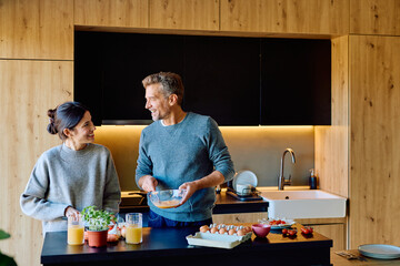 Couple smiling and talking while cooking together, preparing eggs and fresh vegetables for a healthy morning meal in kitchen
