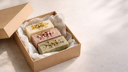 Gift box with organic handmade soap bars decorated with dried flowers. Elegant spa-inspired product flat lay in soft light.