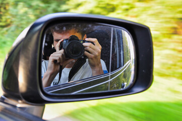 Fotograf siedzący za bocznym lusterkiem samochodu uchwyca jego odbicie podczas jazdy. Kreatywny portret podróżniczy w ruchu, widziany przez boczną szybę. © Pol Badger