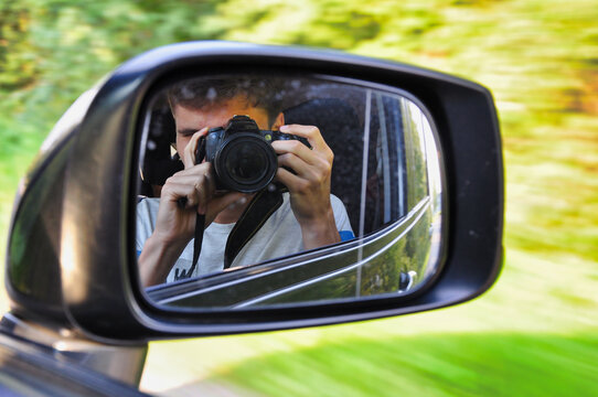 Fotograf siedzący za bocznym lusterkiem samochodu uchwyca jego odbicie podczas jazdy. Kreatywny portret podr&oacute;żniczy w ruchu, widziany przez boczną szybę.