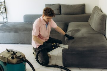 Man dry cleaning sofa upholstery with professional equipment