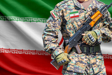 Naklejka premium Iran flag with soldier in military uniform holding assault rifle in front of it