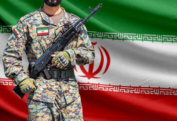 Naklejka premium Iran flag with soldier in military uniform holding assault rifle in front of it