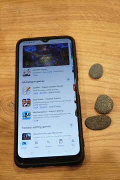 Smartphone displaying a list of mobile games on a wooden table surface
