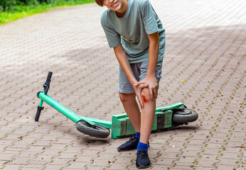 Boy worried about leg injury. Scooter. Blood and scratched skin. Concept of summer holidays. Young boy holding his injured knee after falling off a scooter © Yevhen
