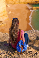 Woman tourist sitting on cliff enjoying beautiful view of paradisiac beach in Algarve, Portugal