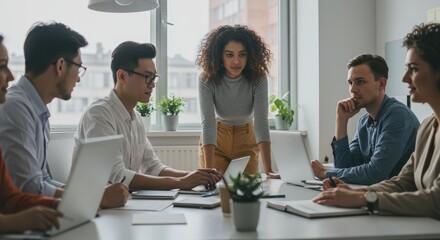 Diverse Team Collaboration: Curly-Haired Woman Leads Meeting with Laptops and Natural Light