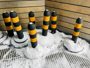 Flexible bollard. Traffic bollards covered in snow against a wooden backdrop in a winter setting. Winter time. 