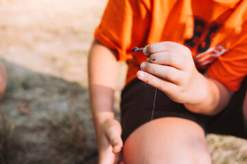 A boy in an orange shirt holding a worm as fishing bait in his hand, preparing for fishing