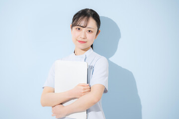 Nurse holding a computer or tablet against a light blue background, looking directly at the camera Image for job changes or recruitment