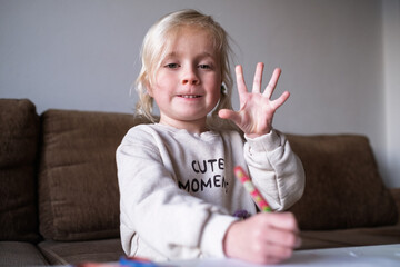 Cute blonde 4 year old girl showing five fingers or high five gesture.