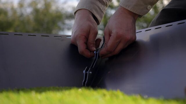 close-up of two Caucasian men's hands screwing a bolt onto a metal bracket outdoors