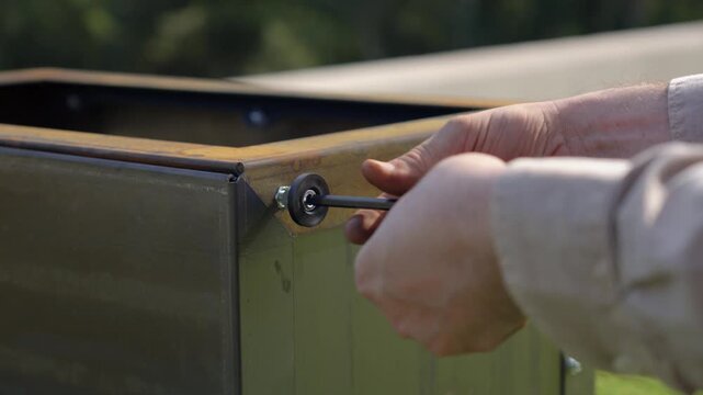 close-up of Caucasian man's hands screwing a bolt into a metal plate outdoors on a sunny day