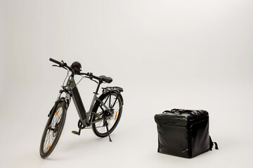 Electric bike rests beside a black delivery bag in a plain studio setting with a white background