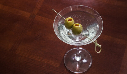 Martini with olives served in a glass on a wooden table in a bar setting during evening hours