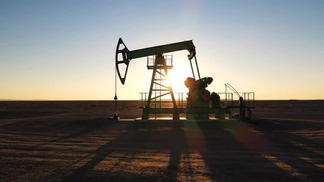 Golden sunlight shining behind a silhouetted oil pump jack working tirelessly in a vast, arid field, representing the continuous extraction of fossil fuels for global energy consumption