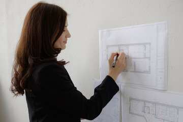 Woman reviewing architectural plans and making notes in an office setting during the day