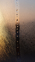 Close-up of water droplets on a foggy glass surface during sunset.