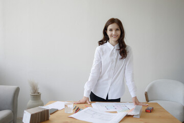 Young woman smiles while standing at desk with work materials in bright office space during daytime