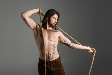 Stylish man with tattoos expressing creativity through rope art indoors