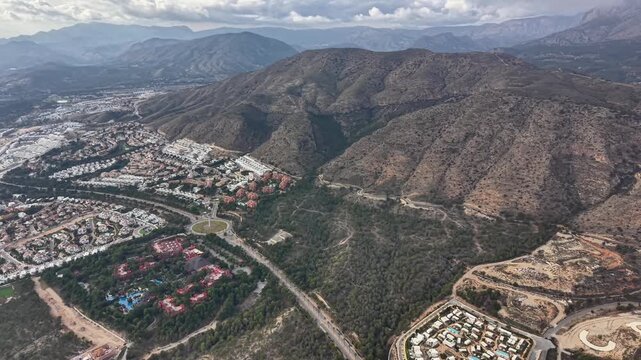 Aerial resort cluster nestled on sunbaked hills, tiled roofs and pool complexes, curving roads and new