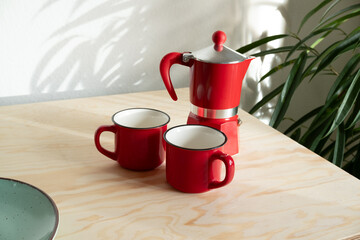 Red Moka Pot and Matching Coffee Mugs on Plywood Surface with Plant