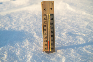 A wooden thermometer in the snow measuring the cold winter outdoor temperature.