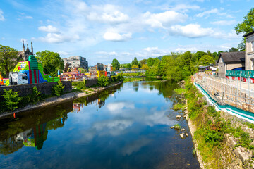 Fototapeta premium Kendal, ville du Lake District, avec rivière, reflets et fête foraine colorée au printemps, Cumbria, Angleterre