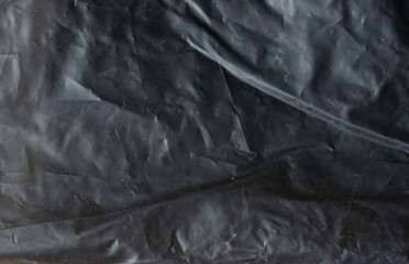 Grunge black plastic texture with chaotic creases and scratches, abstract dark background for creative design use.