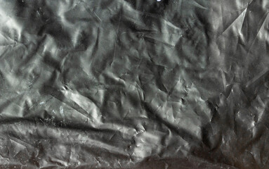 Dark abstract crumpled plastic texture with dramatic lighting, rough surface details, and modern industrial grunge background.