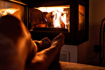 A pair of feet in front of the fireplace. A woman and man warm themselves by the fire.