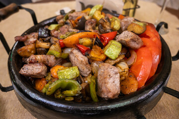 An authentic Bulgarian Sach dish, showcasing grilled meat and colorful vegetables like zucchini, bell peppers, and tomatoes, served hot in a rustic clay pot in Bansko, Bulgaria © Danica Chang