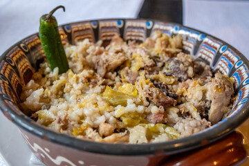 A close-up of a hearty kapama stew, featuring rice, various meats, and cabbage, garnished with a green chili in an authentic patterned ceramic bowl in Bansko, Bulgaria.