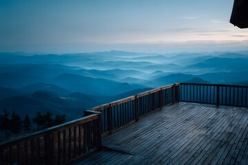 Fototapeta premium View from a wooden deck with railing, overlooking a vast mountain range covered in morning mist, layers of blue mountains fading into distance.