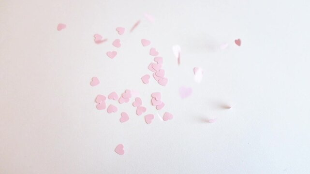 Heart shaped paper confetti falling on white paper background. St. Valentines Day romantic surprise, wedding decor, flying hearts, falling in love concept. Closeup slow motion video.