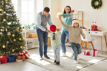 Happy united family dancing near decorated Christmas tree, enjoying festive mood together. Joyful parents and children having fun during Christmas holidays at home. Merry Christmas, Happy New Year.