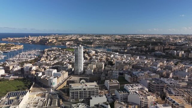 Aerial view of Ta' Xbiex and Valletta, Malta, featuring a bustling marina, urban architecture, and the Mediterranean Sea beneath a clear blue winter sky.