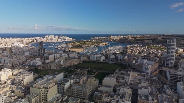 Orbital drone view over Malta's urban coastline, highlighting Msida, Ta' Xbiex, Sliema, and Valletta areas with a bustling Mediterranean marina with boats, yachts, and scenic architecture.