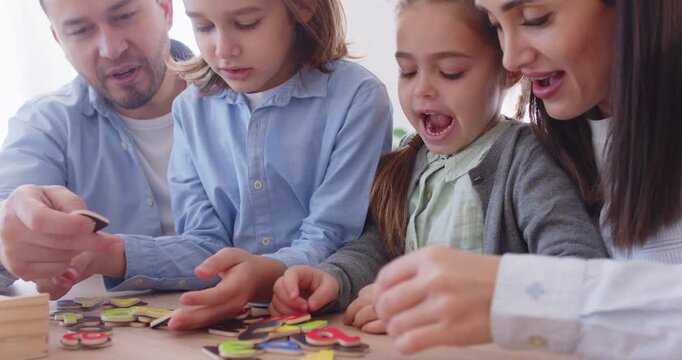 Positive parents and kids spend family leisure time together at home, sitting at desk, learning letters and playing fun educational games to foster bonding and a love for the alphabet.