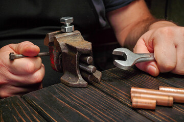 A person uses a wrench and a small clamp to tighten a metal piece while additional copper pipes are...