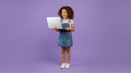 Joyful child engaged with laptop studio setting digital interaction purple background full-body view learning experience