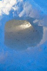 Inside a small snow tunnel or igloo with bright light at the end