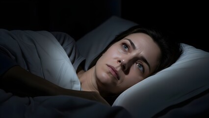 A young woman experiencing anxiety at night while a man lies in bed.,JPGSTOCK .../