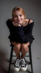 Jeune femme blonde souriante assise sur une chaise en pull noir