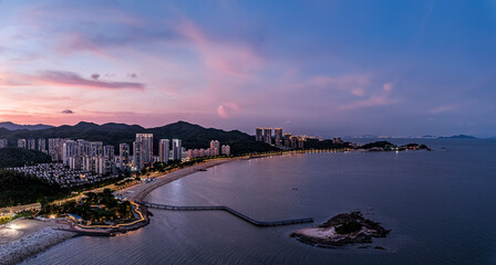 Vibrant aerial view of a modern coastal city skyline and beach at sunset with mountains in Zhuhai.