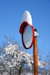 Red convex traffic mirror covered with snow against blue sky